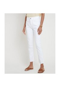 Jeans in denim bianco con una vestibilità slim, lunghezza cropped e orlo sfilacciato. Abbinati a sandali con fascia intrecciata di colore marrone.