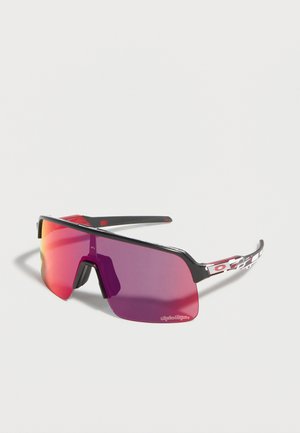 Sportsna wraparound sončna očala s svetlo vijolično-roza ogledalno lečo, črnim okvirjem in vzorčastimi črnimi, belimi in rdečimi kraki na svetlem ozadju.