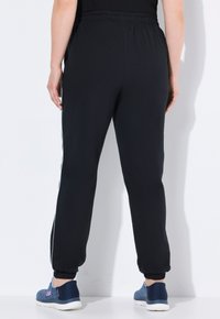 Schwarze Sporthosen mit einem elastischen Bund und schmal zulaufenden Bündchen, ausgestattet mit weißen seitlichen Streifen und einem glatten, leichten Stoff.