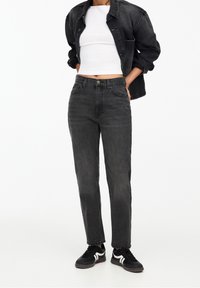 Svarta denimjeans med rak passform, hög midja och blekt utseende. Matchas med en vit kort topp och svarta sneakers.