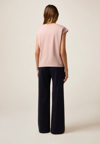 Rosa kurzärmliges Oberteil mit lockerer Passform, kombiniert mit weit geschnittenen marineblauen Hosen. Glatte Textur, einfaches Design und keine sichtbaren Muster oder Akzente.