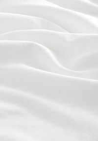 Weißer Stoff mit einer glatten, weichen Textur, der sanfte Wellen und Falten aufweist und seine leichte und luftige Qualität unterstreicht.