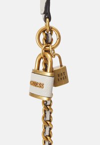 Catena in metallo dorato con un lucchetto in pelle bianca che presenta il logo "GUESS" e un lucchetto con dettagli dorati contrassegnato "EST 1981."