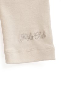 Pantaloni in cotone beige con una vestibilità aderente e logo ricamato "Polo Club" in filo grigio chiaro vicino all'orlo. Tessuto morbido e design semplice.