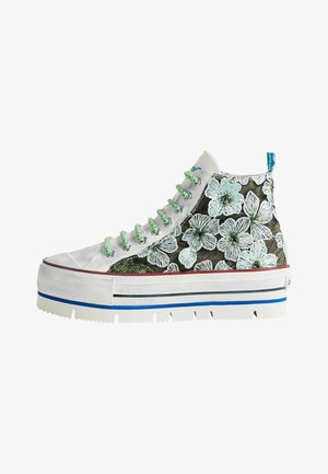 Zapatilla de caña alta con suela blanca gruesa, cordones verdes y azules, y bordado floral verde sobre fondo de tela negra.