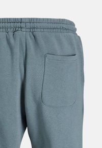 Pantalones de chándal azul claro con cintura elástica, que cuentan con un bolsillo de parche en el lado trasero derecho y una textura suave y lisa.