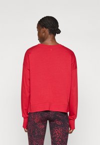 Felpa rossa con una vestibilità rilassata, scollatura rotonda e maniche lunghe. Presenta polsini a costine e un orlo leggermente accorciato. Abbinata a leggings stampati.