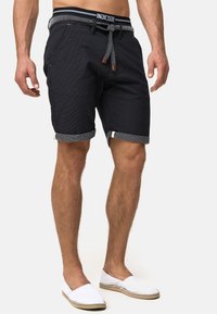 Sorte mønstrede shorts med opkrøllede bukseben og en snor i taljen, parret med hvide slip-on sko. Justerbar talje med detaljer.