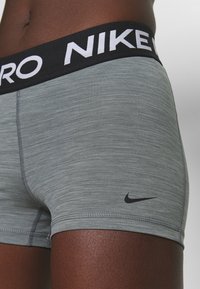 Gray athletic shorts with a black elastic waistband featuring "NIKE PRO" in white text. Black Nike logo on the lower side.