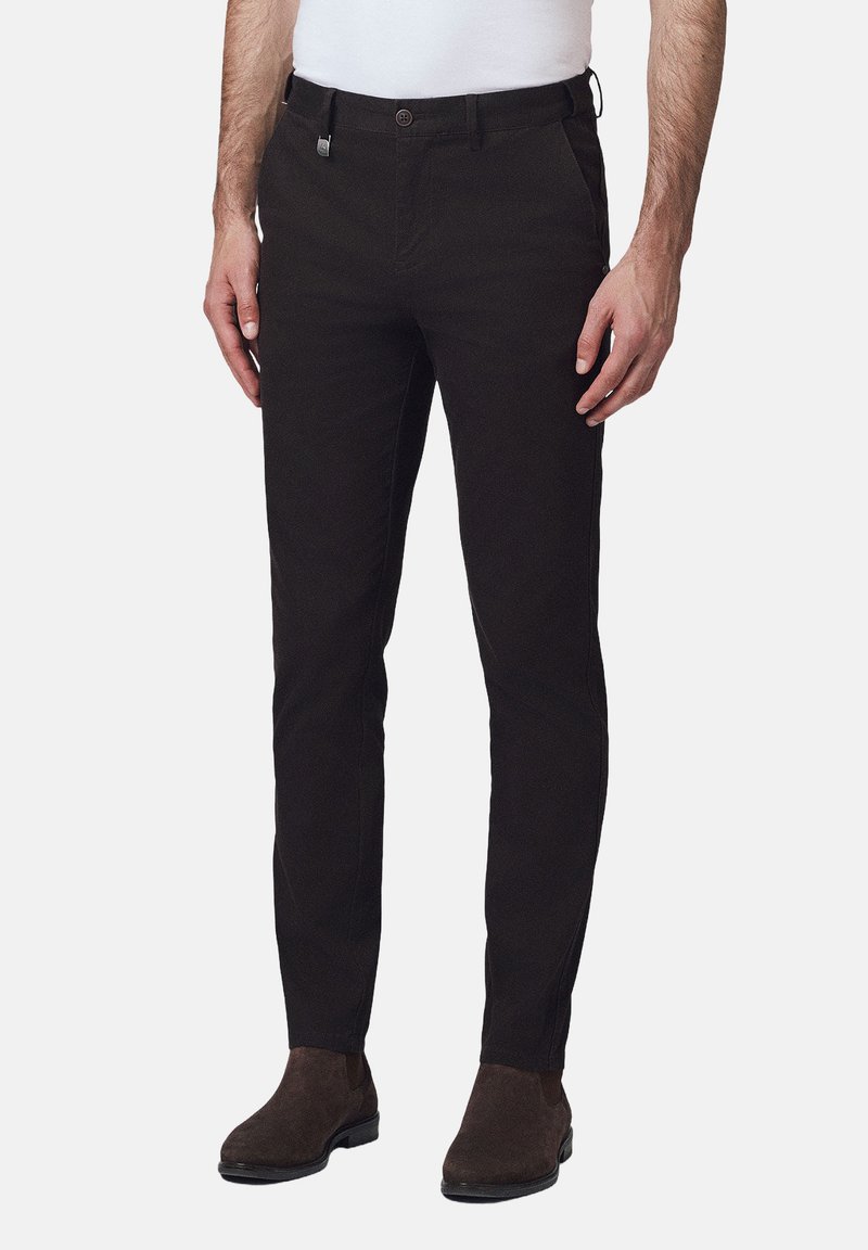 Czarne bawełniane spodnie o slim fit, z zapięciem na guzik, zamkiem błyskawicznym i kieszeniami z przodu, zestawione z brązowymi zamszowymi botkami za kostkę.