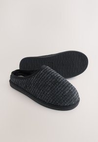 Chaussons tricotés noirs et gris avec un bout arrondi, une doublure en polaire et une semelle en caoutchouc texturée présentant un motif ondulé.