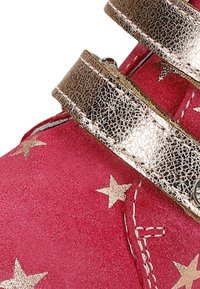Růžová semišová bota se zlatými metalickými hvězdnými vzory a dvěma širokými lesklými zlatými pásky. Výrazné stehové detaily podél okrajů.