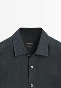 Dark gray linen button-up shirt with a pointed collar and visible white buttons on a white background.