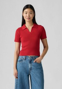 Röd ribbad pikétröja med korta ärmar och V-ringning, tillsammans med högmidjade ljusblå jeans. Slät textur, figurnära stil.