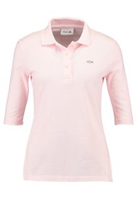 Světlé růžové polo tričko vyrobené z texturované tkaniny, s trojím knoflíkovým zapínáním, krátkými rukávy a vyšitým logem na hrudi.