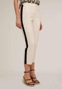 Beige kroušed trankolit s černými bočními pruhy, hladká textura, přední kapsy, nošeny s černými sandály na klínku se strappy.