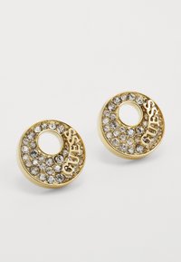 Orecchini circolari d'oro con un ritaglio centrale, adornati con cristalli trasparenti e impreziositi dalla parola "GUESS".