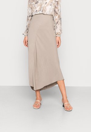 Woman wearing a beige asymmetrical midi skirt, marble-patterned long sleeve blouse, and strappy cream heeled sandals.