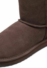 Bruine suède enkelboot met een ronde neus, zichtbare stiksels en een rubberen zool met een gestructureerd patroon voor grip.
