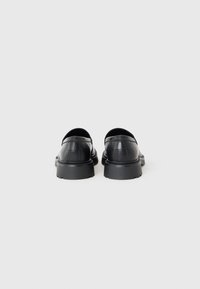 Black leather shoes with a rounded toe, low-profile design, and textured surface. Features a chunky black sole and subtle stitching details.