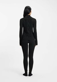 Czarna bluzka z długim rękawem i legginsy z teksturowanymi wzorami w kształcie diamentów. Tkanina wygląda na gładką, dopasowaną i bezszwową, bez widocznych zapięć.