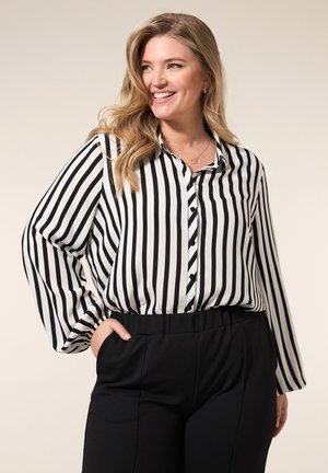 Zwart-wit gestreepte blouse met een knoopsluiting aan de voorkant, lange mouwen en een relaxte pasvorm, gecombineerd met hoge zwarte broeken.