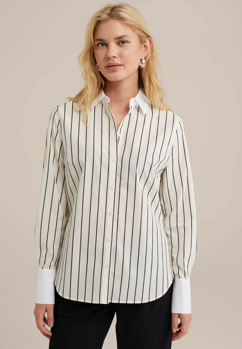 Camicia bianca con strisce verticali nere, maniche lunghe, colletto bianco e dettagli bianchi ai polsini. Presenta un orlo curvo.