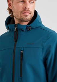 Teal softshell jacket with a zippered chest pocket, adjustable drawstring hood, and stitching details. Features TOG24 logo in black.