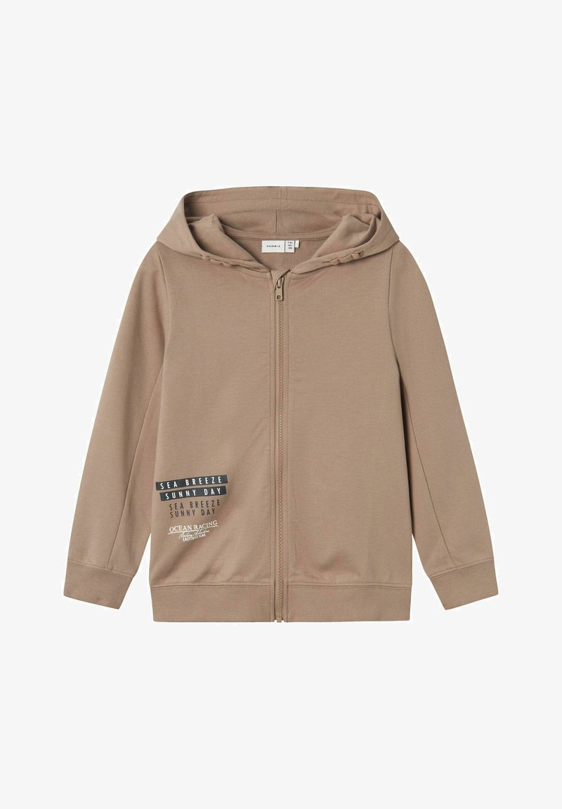 Felpa con zip di colore beige realizzata in materiale morbido. Presenta un cappuccio con cordino, maniche lunghe e una grafica stampata sul lato sinistro.