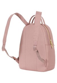 Jasnoróżowy plecak z tkaniny o zaokrąglonym kształcie, złotym zamek błyskawiczny, dwie regulowane ramiączka oraz kieszeń boczna dla dodatkowej przestrzeni na drobiazgi.