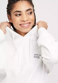 Biała bluza z kapturem z kieszenią kangurzą, z regulowanym kapturem i nadrukowanym tekstem po lewej stronie. Miękki materiał o luźnym kroju.
