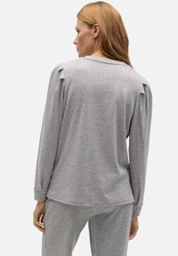 Top gris de manga larga con una textura suave, que cuenta con un cuello redondo y un ligero volumen en los hombros. Combinado con pantalones grises a juego.