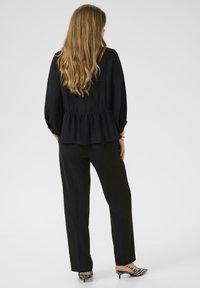 Black peplum blouse with billowy sleeves paired with black tailored pants. Model wears striped high-heeled shoes, hair cascading down.