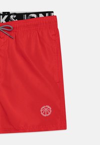 Pantaloni da bagno rossi con cintura elastica e lacci. Presentano tasche laterali e un logo bianco di palma sull'orlo inferiore.