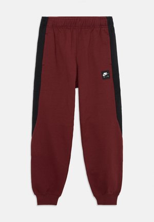 Bordové tepláky s černými bočními panely, elastickým pasem a malou černou nášivkou Nike Air na levé noze. Měkká textilie.