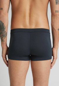 Bóxer oscuro de color navy, hechos de una tela suave, con una cinturilla sin costuras y un ajuste ceñido. Textura lisa sin patrones visibles.