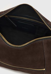 Brūnas zamšādas rokas somas iekšpuse ar melnu oderi. Aprīkota ar zelta rāvējslēdzēju un mazu kabatu. Minimālistisks dizains ar gludu tekstūru.