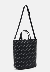 Černá taška přes rameno s nastavitelným popruhem a krátkými uchy, zdobená diagonálními logy "Tommy Jeans" ve světle šedé barvě.