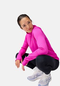 Rožinė ilgomis rankovėmis sportinė maikutė su tekstūruotu raštu; derinama su juodomis tamprėmis ir šviesiai pilkais bėgimo batais, demonstruojant sportišką išvaizdą.