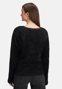 Czarny, puszysty sweter z szerokim dekoltem, długimi rękawami i prążkowanym dołem. Miękka faktura o przytulnym wyglądzie. Widoczny od tyłu.