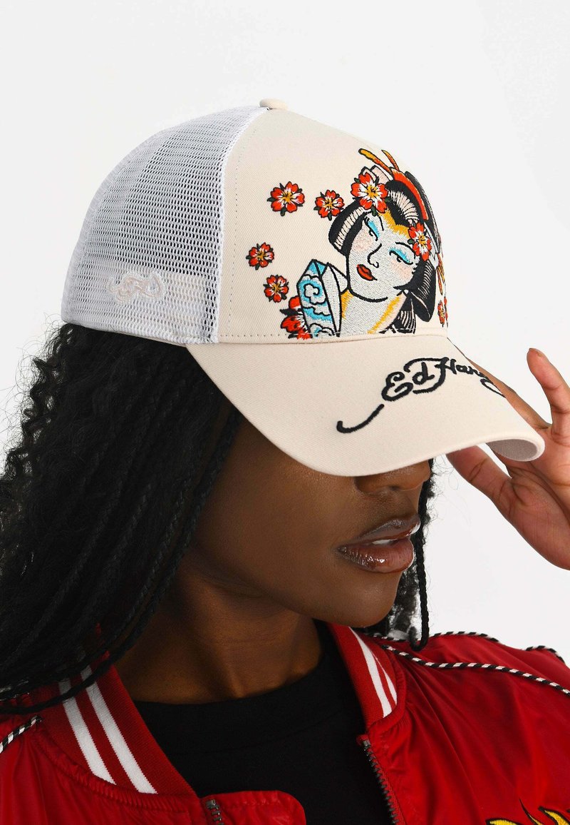 Lastbilskepan har en krämfärgad front med broderad blommönster och Geisha-design, vit nätbakgrund och "Ed Hardy"-logotyp på skärmen.