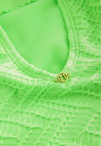 Maillot de bain vert avec un design texturé et orné de motifs. Détail de fermeture en métal doré au niveau du col. Tissu lisse et extensible.