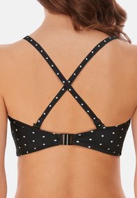 Sort bikini top med hvide diamantmønstre, krydssnore og en hægte lukning bagpå. Glat tekstur og justerbare stropper.