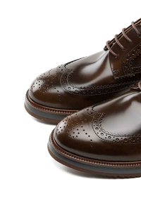 Chaussures brogues en cuir marron présentant une finition lisse, des perforations décoratives et un bout arrondi. Design à lacets avec une semelle contrastante.