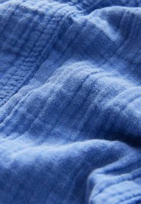Gestructureerde blauwe stof met subtiele variaties, met een zachte, lichte uitstraling en fijne, lineaire stikdetails.