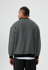 Sweat-shirt à rayures noires et blanches avec une coupe ample, des poignets côtelés et un ourlet noir uni. Tissu doux, vu de dos.
