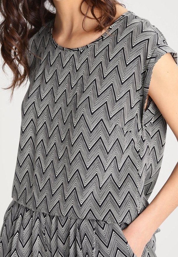 Femme portant un haut sans manches à motif zigzag noir et blanc et un bas assorti, main dans la poche.