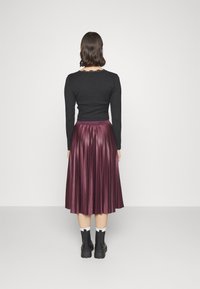 Top aderente nero con maniche lunghe, abbinato a una gonna plissettata bordeaux lunghezza ginocchio. La modella indossa stivali neri chunky.