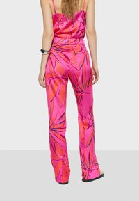 Roze satijnen jumpsuit met bloemenprint, met dunne bandjes en een aansluitende taille die uitloopt in wijde broekspijpen. Soepele textuur en levendige kleuren.