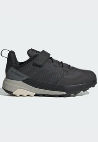 Zapatilla deportiva negra con parte superior de malla y sintético, que cuenta con una correa de velcro, suela texturizada y una entresuela gris para mayor tracción.